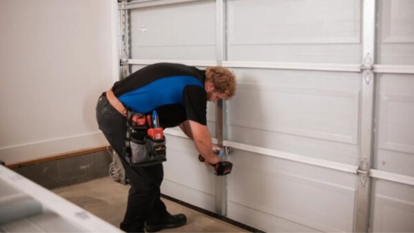 Technician repairing lower panel of residential garage door with power drill