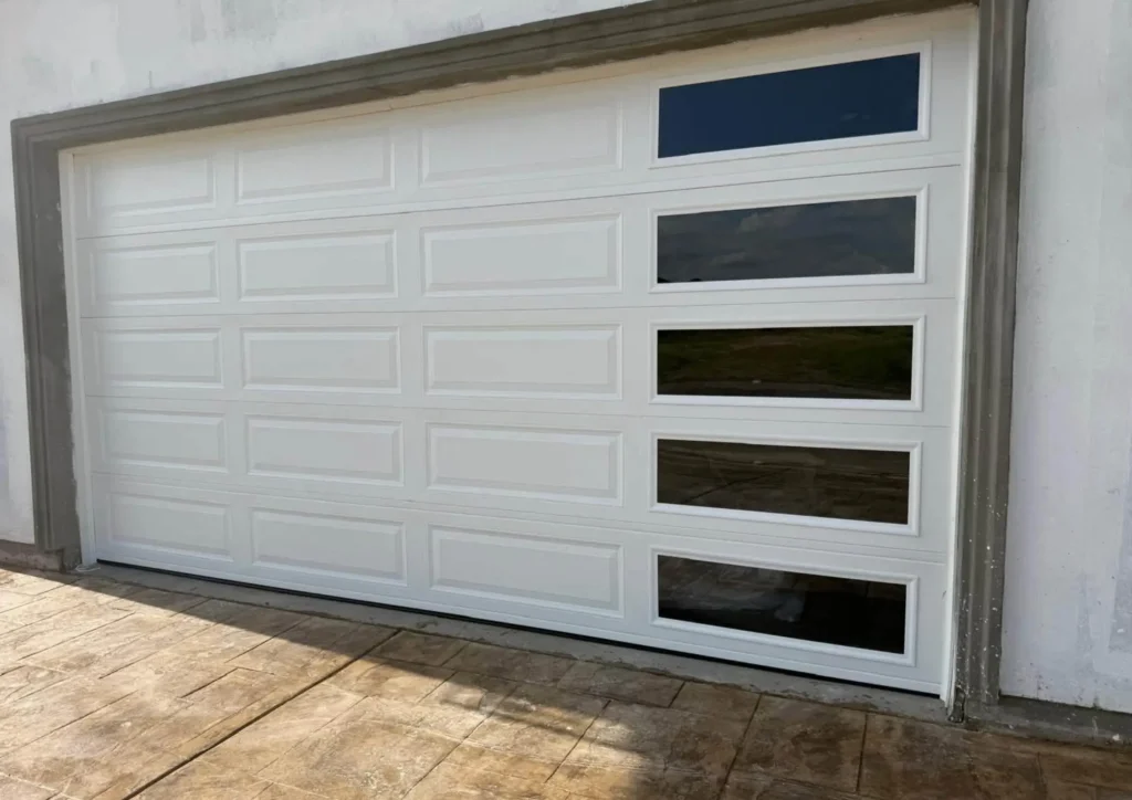 Newly installed white raised-panel garage door with side window panes on a stucco home in Dinuba, CA
